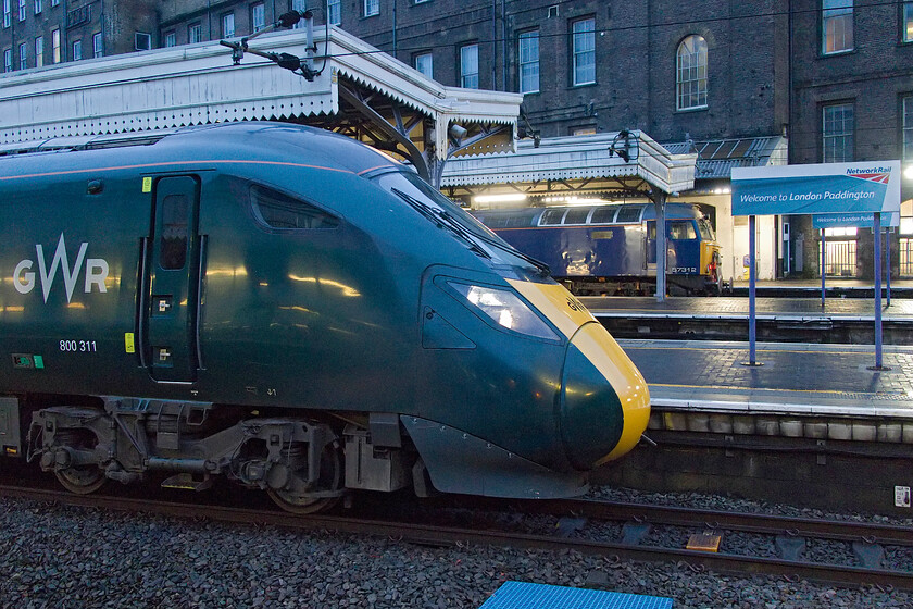 800311, GW 07.00 London Paddington-Bristol Temple Meads (1C03, RT) & 57312, 07.34 London Paddington-Reading Traincare Depot (5A50, 5L), London Paddington station 
 A dismal early morning scene at Paddington sees 800311 preparing to leave with the 07.00 GWR service to Bristol Temple Meads. Behind the IET on platform one, 57312 waits to depart half an hour or so later at 07.34 with the sleeper empty coaching stock. With the closure of Old Oak Common due to HS2 developments, the 5A50 runs much further west to Rading Train Care Depot where it is serviced and stabled before returning in the evening for the next down service to Penzance. 
 Keywords: 800311 07.00 London Paddington-Bristol Temple Meads 1C03 57312 07.34 London Paddington-Reading Traincare Depot 5A50 London Paddington station GWR Great Western Railway sleeper