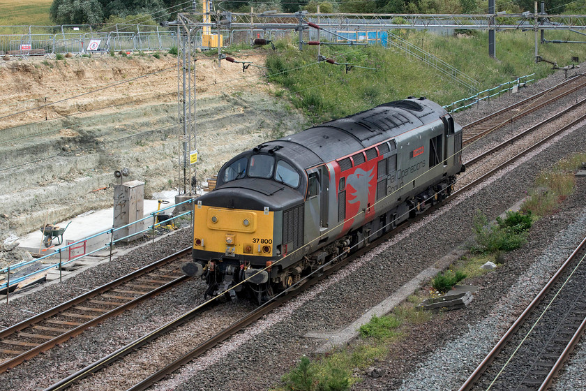 37800, 12.20 Ilford EMUD-Leicester LIP (0Z , 52E), Ashton Road bridge 
 As is becoming the norm now, the 12.20 Ilford to Leicester light engine move was running very early eventually arriving at its destination nearly an hour up. 37800 'Cassiopeia' is about to pass under Ashton Road bridge just south of Roade after delivering a former GA Class 315 from Kilmarnock earlier in the day following an overnight stopover in Wembley Yard. As can be seen in the background, the work to stabilise the embankment at this location is moving painfully slowly forward following the tragic death of a contractor at this site back at the beginning of April. By now all works should have been completed and the access land returned to the farmer. 
 Keywords: 37800 12.20 Ilford EMUD-Leicester LIP (0Z??, 52E), Ashton Road bridge Cassiopeia light engine Rail Operations Group ROG Europheonix