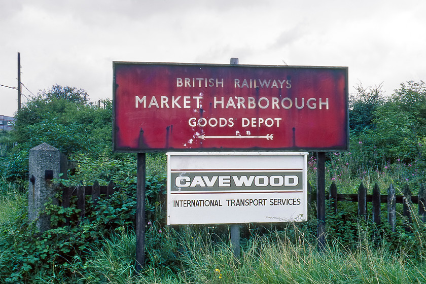 Enamel, Market Harborough Goods Yard entrance 
 A large BR (London Midland) enamel near to Market Harborough station pointing to the closed goods depot. The sign for Cavewood International Transport Services is a little bit of a mystery as a haulage company by this name exists still today but in High Wycombe. Their logo is very similar to the one on the sign so perhaps this was a sub-depot; can anybody advise? Interestingly, this view is still possible today with the road to the left off Rockingham Road leading to a number of business units. All has changed but the road still exists with the telegraph poles being the only reference points, see..... https://www.ontheupfast.com/p/21936chg/30017882655/x9-former-ggod-yard-entrance-market 
 Keywords: Enamel Market Harborough Goods Yard entrance