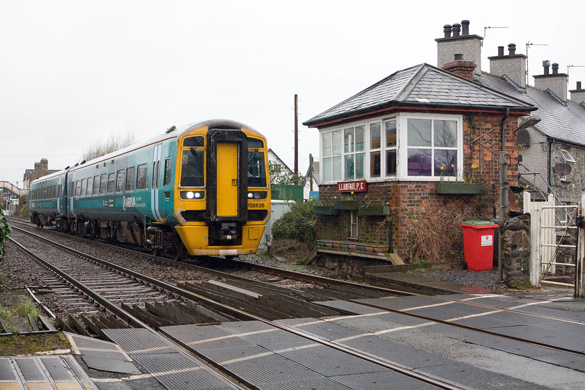 158836, AT 09.23 Holyhead-Birmingham International (1G32), Llanfair level crossing 
 158836 passes Llanfair level crossing and signal box working the 09.23 Holyhead to Birmingham International. This box is believed to be the only surviving example of a gate box used for controlling the adjacent level crossing in Wales. The station can be seen towards the back end of the train. 
 Keywords: 158836 09.23 Holyhead-Birmingham International 1G32 Llanfair level crossing