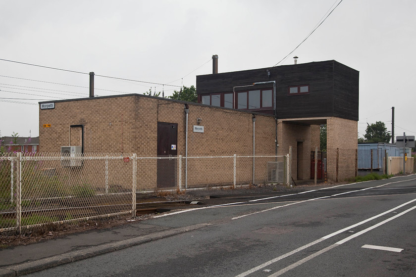 Morpeth signal box (BR, 1978) 
 The rather utilitarian structure that is Morpeth signal box is seen from the rear. It is located just north of the station at the point where the complex of freight-only lines to Blyth and Ashington diverge from the ECML. Indeed, the southern link to these lines is seen crossing the road in the foreground with the BR built 1978 box behind. The overhead electrification wiring of the ECML is seen behind the box. 
 Keywords: Morpeth signal box