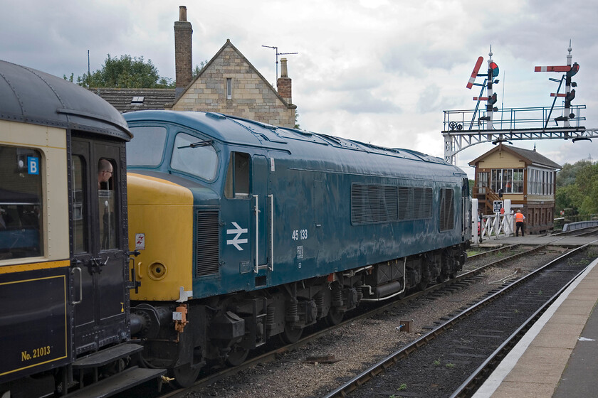 45133, 12.42 Wansford-Peterborough Nene Valley (2E49), Wansford station 
 Peak 45133 waits to leave Wansford station working the lunchtime 12.42 service to Peterborough Nene Valley. It will pass under the large signal gantry that houses a superb Great Eastern somersault signal that has been pulled off permitting the departure of the train. 45133 was released into traffic in July 1961 as D40 undertaking a variety of duties both freight and passenger. In 1974 it became ETH-equipped and dedicated to Midland mainline work being replaced by the arrival of the HSTs ending its days working Trans Pennine services in May 1987. After languishing along with many other class members at March's Whitemoore Yard it was bought by the Class 45/1 Preservation Society in 1990. 
 Keywords: 45133 12.42 Wansford-Peterborough Nene Valley 2E49 Wansford station Peak