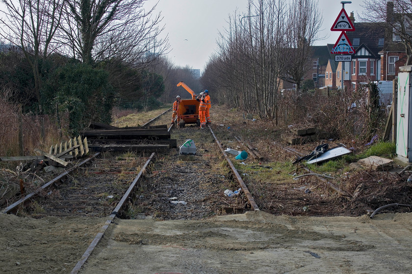 Clearance, Folkestone Harbour branch, Warren Road level crossing 
 Looking south from the old Warren Road level crossing on the Folkestone Harbour branch sees a crew engaged in shredding following extensive clearance of trees and saplings. Unfortunately, this is no precursor to the line being re-opened but so it can be cleared of its infrastructure and put to a new use of which I am unsure. One would hope that it does not become a strip for development or turned into a road but that it performs a useful duty for the community such as a cycleway or walkway down through the town to the renovated harbour area. 
 Keywords: Folkestone Harbour branch Warren Road level crossing