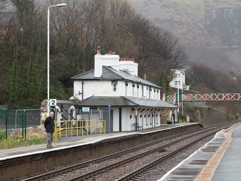 Penmaemawr station 
 Andy stands on Penmaemawr's down platform with the station building the background. The station building, built by the Chester and Holyhead Railway Company in 1850, was sold off by BR in 1986 and subsequently went through a number of uses. This all changed in 2013 when the grade II listed granite-built structure was offered for sale for 127 000. It is now in the hands of its new owner and has had various works undertaken. When I last visited the station in 1981 with Graham the weather was somewhat better than on this miserable April day, see........ https://www.ontheupfast.com/p/21936chg/30035069788/x31-penmaenmawr-station 
 Keywords: Penmaemawr station