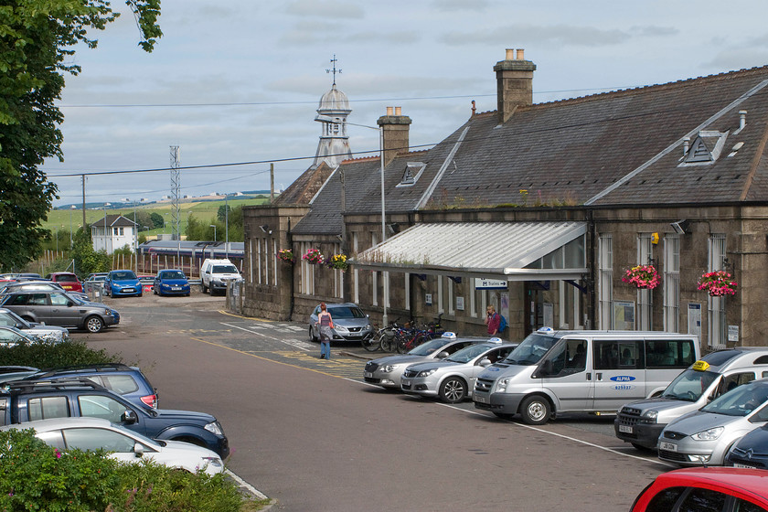 158709, SR 12.00 Aberdeen-Inverness (1H31) & frontage, Inverurie station 
 Whilst the frontage of Inverurie station looks very pleasant with its hanging baskets somebody really ought to get up on the roof and canopy and clear the gutters! The GNS 1902 station building is built of granite to pleasing design complete with an ornate cupola topped with a wind vane. In the background, 158709 leaves the station heading north-west with the 12.00 Aberdeen to Inverness ScotRail service and beyond that this signal box is seen. 
 Keywords: 158709 12.00 Aberdeen-Inverness 1H31 frontage, Inverurie station GNS Railway ScotRail Sprinter