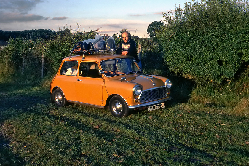 Graham & UAM on his birthday, Burlescombe campsite 
 On his birthday, Graham stands in the evening sunshine at our campsite at Burlescombe behind a well loaded UAM. The West of England mainline is just behind the hedge keeping up our tradition of trying to camp as close to the railway as we could. UAM 736J was to disgrace itself the following day with a split bypass hose that was a common malaise on the A-series engines of the time. Whoever would design an engine with a short rubber cooling hose that required the head to be removed to change it? 
 Keywords: Graham UAM on his birthday Burlescombe campsite UAM736J