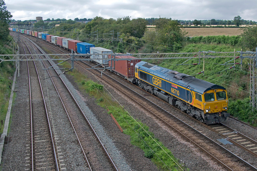 66710, 14.18 Trafford Park-Felixstowe North (4L18, 5E), Victoria bridge 
 66710 'Phil Packer BRIT' brings the well loaded 14.18 Trafford Park to Felixstowe past Victoria bridge just south of Roade. No show from the sun again in this photograph despite large areas of blue sky close by. At least the GBRf liveried Class 66 looks a lot brighter than a Freightliner liveried example. 
 Keywords: 66710 14.18 Trafford Park-Felixstowe North 4L18 Victoria bridge GBRf Phil Packer BRIT