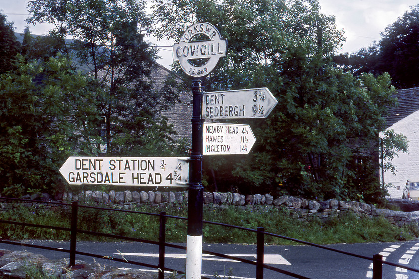 Cast sign, Cowgill (note-Dent Station & GR) 
 I don't normally take photographs of road signs but this one is interesting. It stands in the village of Cowgill at the eastern end of Dentdale at a junction where the road off to the left climbs steeply up to Dent station and then across the moors to Garsdale. The reason for my interest in the sign is that it still points out Dent station despite it having been closed some ten years previously in 1970. Of course, it has subsequently reopened in 1986 as part of the wider renascence of the S & C. Notice that particular arm of the sign has been replaced by a crudely attached section grafted to the stub of the original that has a different font. Even though it shows the station as being a relatively short three-quarters of a mile away, what it does not state is that in that distance, the road climbs nearly five hundred feet with an average gradient of 17% (c. 1:6), with some sections being a lot steeper than that! Using Google Street View today reveals that the sign is still in place complete with its six figure grid reference on the circular topping piece. 
 Keywords: Cast sign Cowgill Dent station