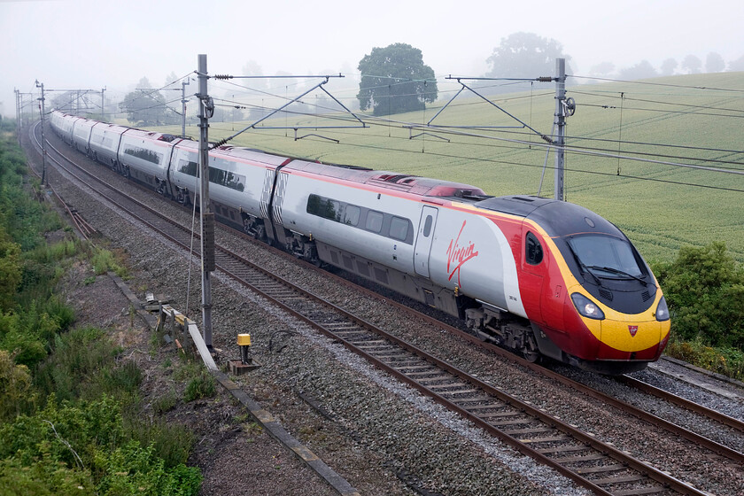 390148, VT 07.23 London Euston-Birmingham New Street (1G05), Blisworth SP735539 
 390148 'Virgin Harrier' sweeps around the first of a number of reverse curves on the Weedon loop line between Roade cutting (about a mile distant from this position) and Hillmorton Junction just south of Rugby. On a foggy and chilly June morning the Pendolino is working the 07.23 Euston to Birmingham New Street Virgin service. 
 Keywords: 390148 07.23 London Euston-Birmingham New Street 1G05 Blisworth SP735539 Virgin Pendolino Virgin Harrier