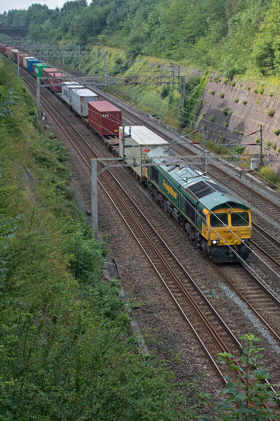 66589, 03.00 Felixstowe North-East Midlands Gateway (4M86, 84E), Roade cutting 
 After continuing my local walk the sun finally began to burn its way through the veil of cloud that enveloped the sky on this mid-summer morning. 66589 leading the 4M86 03.00 Felixstowe North to East Midlands Gateway is in the shade with the sun just illuminating the western wall of the cutting. 
 Keywords: 66589 03.00 Felixstowe North-East Midlands Gateway 4M86 Roade cutting Freightliner