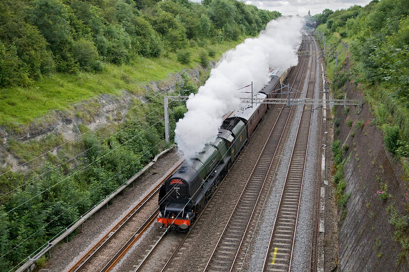 46233, return leg of The Midlander, 17.43 London Euston-Birmingham New Street (1Z87), Roade cutting 
 After its outward non-stop run from Birmingham to Euston in the morning, 46233 'Duchess of Sutherland' returns hauling The Midlander charter. This time there was no non-stop target so it travelled at a more leisurely pace and a different route. Whereas in the morning it took the direct route from New Street via International and Coventry on the return it went via the Trent Valley route to set down at Nuneaton and Coleshill. With a fin display of exhaust, the LMS Princess Coronation Class passes through Roade cutting, something that she will have done many times during her use on the network between 1938 and 1964. 
 Keywords: 46233 The Midlander 17.43 London Euston-Birmingham New Street 1Z87 Roade cutting Duchess of Sutherland