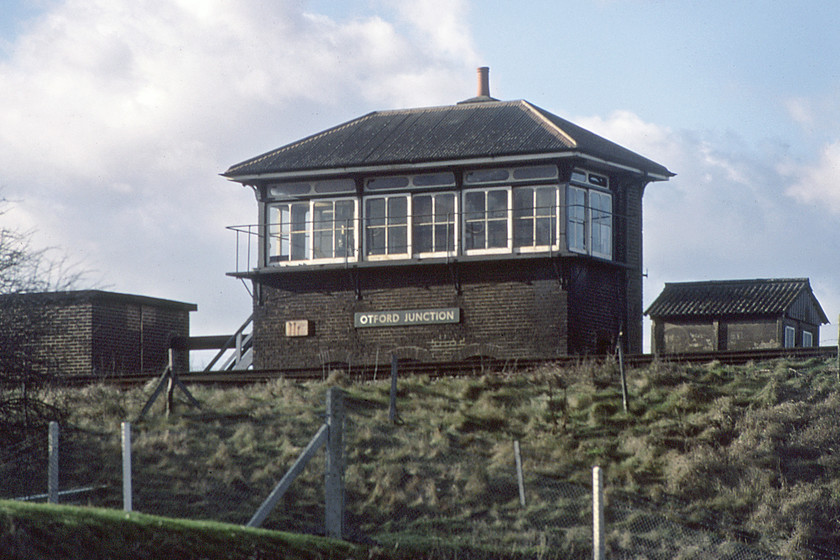 Otford Junction signal box (SE & C, c.1899)-03.01.81 
 Quite how I managed to take this photograph remains a bit of a mystery! It is taken from our coach as we return home from Canterbury to Salisbury as we make our way along the M26 motorway. Had I got my camera in my hand all set up by chance or was I prepared knowing that we would pass it and that it would be in view? We are about to pass under the SE & C line from Swanly Junction to Sevenoaks with Otford Junction signal box seen high on the embankment. The junction is where the Maidstone route heads off to the east. The box retains its attraction Southern wooden name board but the roof has been rather crudely replaced with what appears to be white asbestos sheeting. Opened in 1899, the SE & C box was to close in 1983 with control moving to the Victoria Signalling Centre. 
 Keywords: Otford Junction signal box