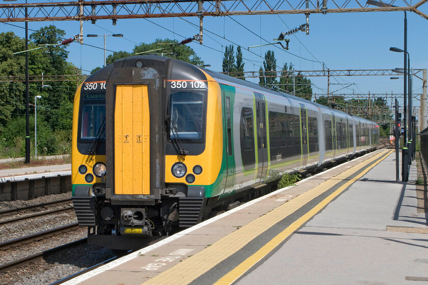 350102, LM 10.14 Birmingham New Street-London Euston (1Y28), Northampton station 
 350102 arrives at Northampton station working the 10.14 Birmingham New Street to Euston 1Y28 London Midland service. The brilliant quality of light on summer days such as this is tempered somewhat by the deep shadows created. I have to use my Photoshop skills to bring back the detail in the shadows to avoid vast areas of blackness as could have been the case in this image's case. Notice the buddleia growing quite happily on the platform edge not appearing to be affected by the extremely close passage of trains! 
 Keywords: 350102 10.14 Birmingham New Street-London Euston 1Y28 Northampton station London Midland Desiro