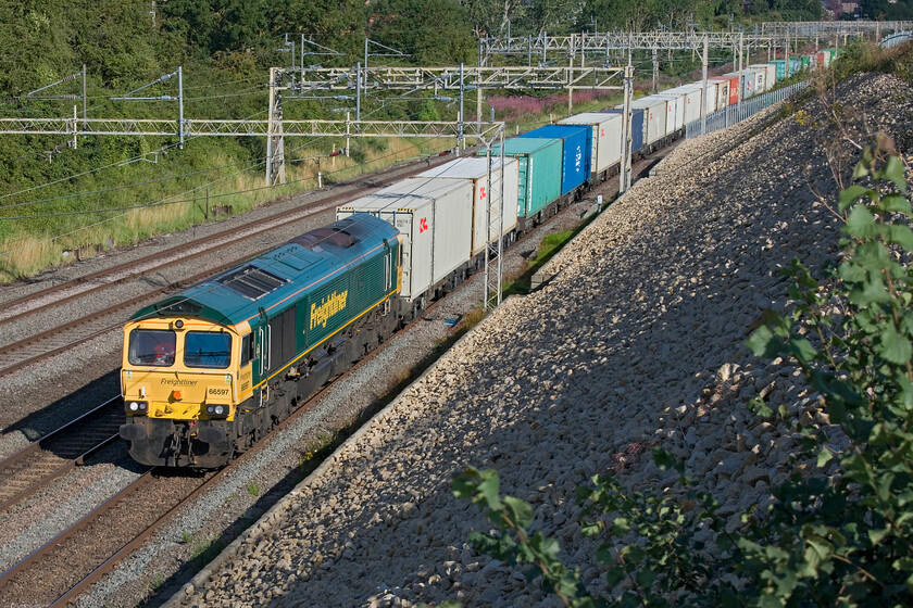 66597, 04.59 Trafford Park-Felixstowe North (4L41, 17E), Ashton Road bridge 
 66597 'Viridor' is about to pass under Ashton Road bridge just south of Roade leading the 04.59 Trafford Park to Felixstowe Freightliner. This spot needs some pruning du to the growth of the bush in the foreground. Indeed, after this photgraph was taken and having my tools in the car, I was able to do some cutting back but need to return again soon. 
 Keywords: 66597 04.59 Trafford Park-Felixstowe North 4L41 Ashton Road bridge Freightliner Viridor