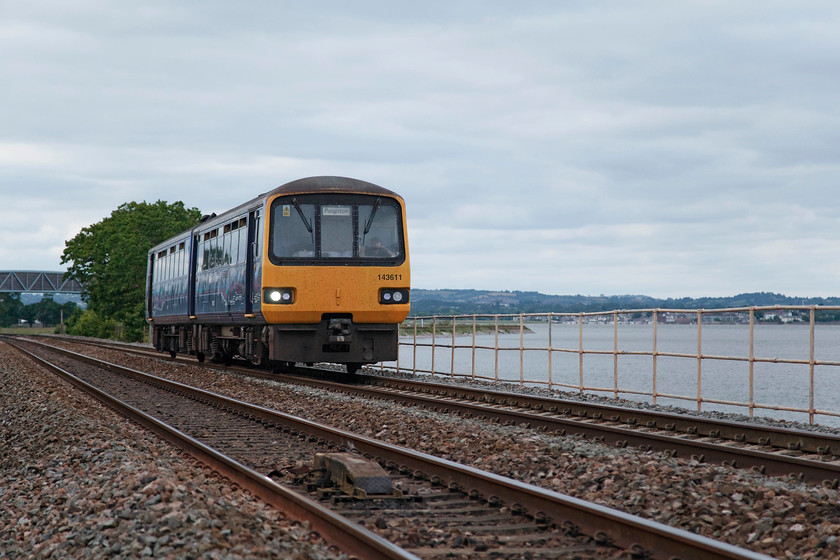 143611, GW 17.46 Exeter Central-Paignton (2T25, 2E), Powderham SX972844 
 I deliberately kept the train off-centre in this image so the lovely Exe Estuary could be seen. 143611 forms the 17.46 Exeter Central to Paignton 2T25 stopper. It is passing Powderham. In the background is the huge Powderham footbridge that carries the Exe Estuary Trail over the railway. It replaced the gated foot crossing that I took a picture of 50047 'Swiftsure' from when undertaking my bike tour of the west of England line in 1979. 
 Keywords: 143611 2T25 Powderham SX972844