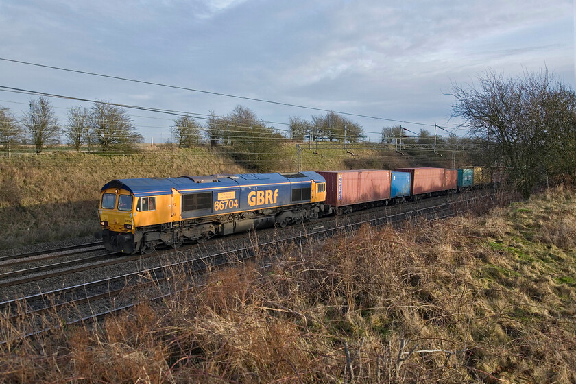 66704 unidentified Freightliner (4M23?), Roade Hill 
 After the dullness of the morning session on the MML near Bedford having moved to the WCML near to home at Roade the sun has come out. In the weak afternoon sunshine GBRf's 66704 'Colchester Power Signal Box' heads north with an unidentified Saturday afternoon Freightliner service.

UPDATE.....Looking at Network Rail's excellent resources in 2023, which include the working timetables, have me believe that this was the 4M23 10.17 Felixstowe to Hams Hall service that was a GBRf-operated working and due at about this time in the afternoon; I stand to be corrected though! 
 Keywords: 66704 Freightliner, Roade Hill GBRf Colchester Power Signal Box