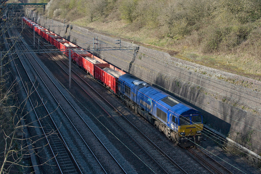 66005, 10.00 Dowlow Briggs-Theale Hope Cement (6V11, 100L), Roade cutting 
 66005 'Maritime Intermodal One' leads the heavy 10.00 Dowlow to Theale 6V11 through Roade cutting conveying white limestone from the Peak District to west London. With the Maritime blue livery and rake of red DB branded MMA wagons, the scene is certainly a different one to the usual procession of Freightliner workings. Unfortunately, soon after this photograph was taken this train failed just south of Wolverton station blocking the up slow line. On any other day, this would have caused absolute chaos but with the emergency timetable in place, control was able to move trains from line to line pretty easily without too many delays. Later in the evening, the train was rescued by 66172 that hauled it to Bletchley. Later still it got on its way arriving a mere two hundred minutes late to Theale. 
 Keywords: 66005 10.00 Dowlow Briggs-Theale Hope Cement 6V11 Roade cutting Maritime Intermodal One Crushed limestone