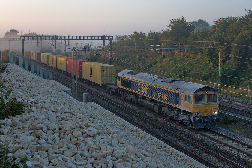 66716, 03.10 Felixstowe North-Trafford Park (Cancelled from Crewe Basford Hall) (4M18, 1E), Ashton Road bridge 
 66716 'Locomotive & Carriage Institution Centenary 1911-2011' emerges from the autumnal mist as the sun just breasts the horizon to the east that is not able to illuminate the train just yet! The 4M18 03.10 Felixstowe to Trafford Park is seen approaching Roade in Northamptonshire that, later in its journey was terminated early on arrival at Crewe Bashford Hall. It appears as if 66716 has been involved in hauling a stone train of some kind given the extensive white dust adoring its leading cab. 
 Keywords: 66716 03.10 Felixstowe North-Trafford Park Crewe Basford Hall 4M18 Ashton Road bridge GBRf Locomotive & Carriage Institution Centenary 1911-2011