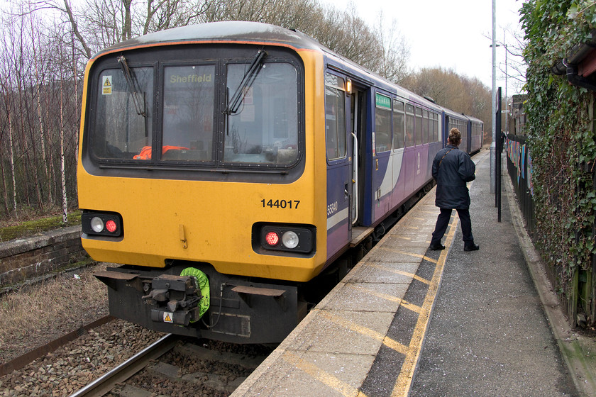 144017, NT 14.12 Huddersfield-Sheffield (2B19, RT), Honley station 
 The guard peers down the platform at Honley station in the vain hope of some passengers, but, to no avail. 144017 waits forming the 2B19 14.12 Huddersfield to Sheffield service. In common with most of the stations on the Penistone Line, they are single platform affairs with some having double tracks to act as convenient passing places. Passenger numbers have been steadily falling at this station over the last few years. Perhaps, the hourly service pattern does not work well for the community? 
 Keywords: 144017 14.12 Huddersfield-Sheffield 2B19 Honley station