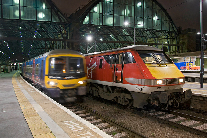 365513, GE 20.44 London King's Cross-Ely (1T16) & 91129, GR 20.49 London King's Cross-Bounds Green TMD ECS (5Y46), London King's Cross station 
 An alternative view of the first photograph in this section at https://www.ontheupfast.com/p/21936chg/29346714404/x82219-20-49-london-king-s-cross sees 365513 leaving King's Cross bang on time with the 20.44 Great Northern service to Peterborough. Next to the Networker, 91129 sits idle waiting to head back to Bounds Green empty as the 5Y46. I like the contrast in this photograph of the motion blur from the Great Northern train compared with the brilliant sharpness and light of the rest of the image aided by the modern LED lighting at the station. 
 Keywords: 365513 20.44 London King's Cross-Ely 1T16 91129 20.49 London King's Cross-Bounds Green TMD ECS 5Y46 London King's Cross station Great Northern VTEC Virgin Trains East Coast