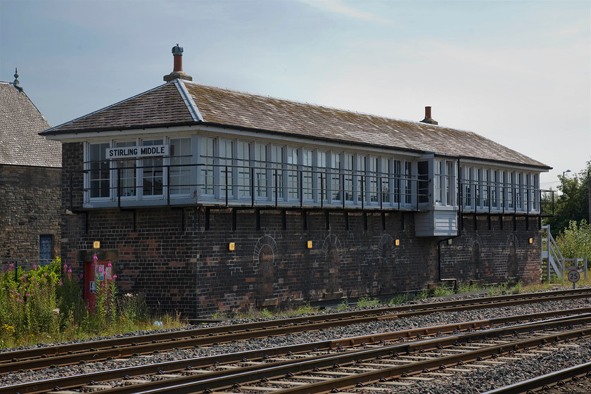 Stirling MIddle signal box (Caledonian, 1901) 
 I knew that I had taken my trusty step ladder all the way to Scotland on the sleeper and then in the back of two hire cars for a reason! I put it to good effect here to get a bit of height to capture Stirling Middle signal box. It's horribly back-lit but positions to get a picture was somewhat limited. The superb 1901 Type 2 Caledonian box now had been modified from operating a super suite of mechanical signals to a modern set of colour lights. This is a temporary measure whilst the electrification of the lines takes place. The box is a classic design complete with its two chimney stacks and wooden nameboard. Notice the two-bays projecting to right of centre that would have allowed the signalmen to view, flag and communicate with drivers without having to walk to the far end of the lengthy box. It's a shame that the five locking room windows have been bricked up taking away a little of the boxes character when compared to its North sibling, see.... https://www.ontheupfast.com/p/21936chg/28963914004/stirling-north-signal-box-caledonian 
 Keywords: Stirling MIddle signal box Caledonian