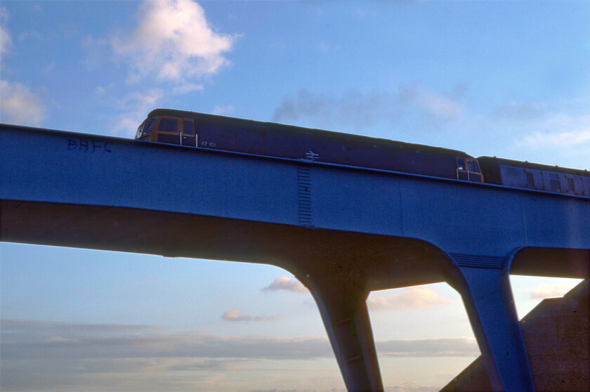 47101, 14.35 Paignton-Leeds (1E70), overbridge, junction 19 of M4 
 A highly unusual photograph taken from the front seat of Mike's Mk. 1 Ford Fiesta as we made our way home along the M4 north of Bristol at the point where the M32 diverges at Junction 19. This bridge that carries the GWML is just east of Bristol Parkway and is exactly the same today even down to its characteristic shade of blue paint the only difference being that it now has electrification masts erected on it. In this view 47101 has just left Parkway station, then a rather faceless and windswept station, leading the 1E70 14.35 Paignton to Leeds train that will soon head north away from the Great Western territory on the Midland route at Westerleigh Junction. Notice the trespasser who has risked life and limb to spray paint his support for Bristol Rovers on the bridge parapet. Having made all that effort I thought that he might have tried to make the letters a little larger! 
 Keywords: 47101 14.35 Paignton-Leeds 1E70 overbridge junction 19 of M4