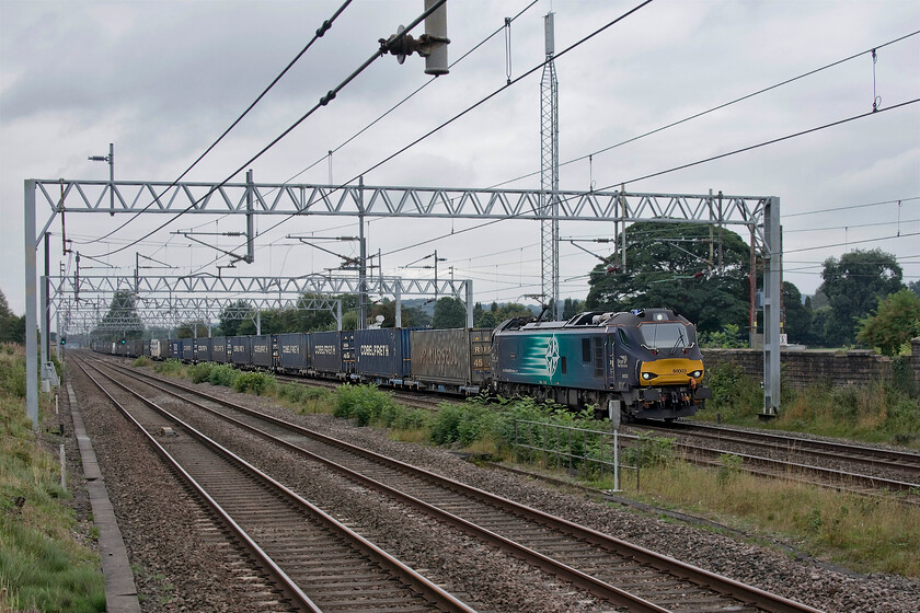 88003, 12.16 DIRFT-Mossend (4S44, 2E), Madeley SJ773439 
 88003 Genesis leads the 4S44 12.16 Daventry (DIRFT) to Mossend intermodal working past Madeley in Staffordshire. The Class of ten locomotives have not all been named as yet but those that have carry names in homage to the EM1 and EM2 DC electric locomotives of the 1950s; a nice touch from their operator Notice the overbridge in the distance, this carries the former North Staffordshire line over the WCML that is still rail connected that was last used back in 1998 to carry coal from Silverdale colliery. 
 Keywords: 88003,12.16 DIRFT-Mossend 4S44 Madeley SJ773439 DRS Direct Rail Services Genesis