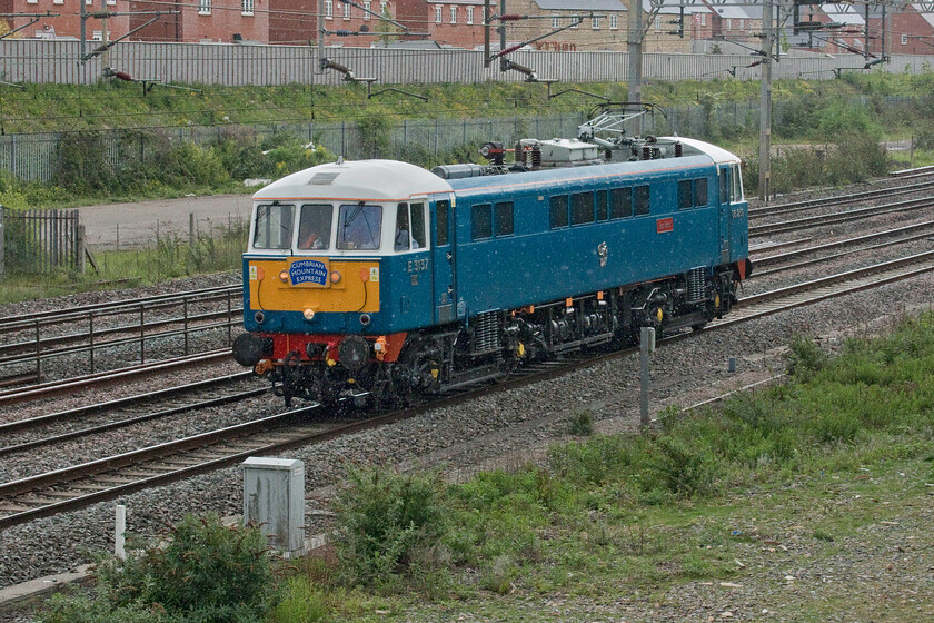 86259, 12.20 Acton Lane-Rugby CS (0Z88, 18L), site of Roade station 
 Still wearing its headboard from yesterday's railtour duties (see..... https://www.ontheupfast.com/p/21936chg/30014872866/x86259-cumbrian-mountain-express) 86259 'Les Ross/Peter Pan' heads north past Roade heading back to its weekday base in some overgrown sidings at Rugby. Running as the 0Z88 12.20 Acton to Rugby it was fairly late due to a delayed departure. Notice that the rain has started again after what had been a pleasantly dry but cloudy Sunday morning. 
 Keywords: 86259 12.20 Acton Lane-Rugby CS 0Z88 site of Roade station Les Ross Peter Pan