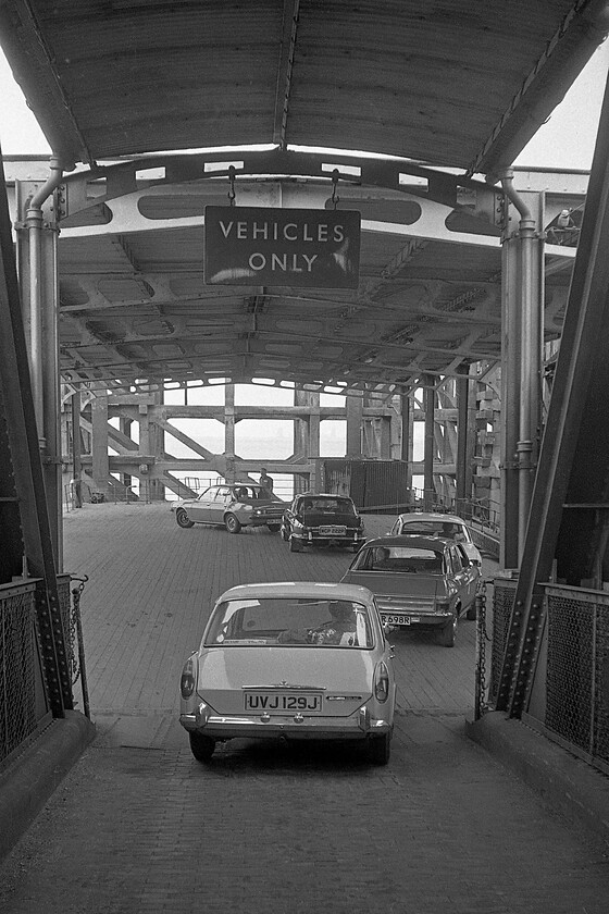 UVJ 129J, loading ramp, New Holland Pier 
 Graham waits on the loading ramp at the wheel of UVJ 129J on New Holland Pier where he will soon join MV Farringford from for the 16.50 sailing to Hull Corporation Pier. Notice that the full lineup of vehicles in this scene are all British with a Mk. 1 Vauxhall Cavalier GLS (even though it was under the control of GM Europe), a very rare Series II Daimler Sovereign that appears to be in two-door form, a Mk. 1 Ford Escort, an Allegro Super and our own Austin 1100 nearest the camera. The huge enamel hanging above the loading ramp is also of interest, I wonder where that ended up a week later when the ferry operations ceased and the pier closed? 
 Keywords: UVJ 129J loading ramp New Holland Pier Sealink