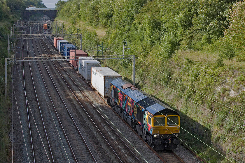 66718, 13.55 Birch Coppice-London Gateway (4L68, 3E), Hyde Road bridge 
 66718 'Sir Peter Hendy CBE' leads the 4L68 13.55 Birch Coppice to London Gateway through Roade cutting seen from the village's Hyde Road bridge. The celebrity liveried GBRf Class 66 carries vinyls promoting transport throughout London in all of its various guises with particular reference to the London Transport Museum. Even back in 2010 when I first saw this locomotive its identity was still associated with TfL wearing striking orange Metronet vinyls celebrating the renewal of the tube and was named 'Gwyneth Dunwoody'. 
 Keywords: 66718 13.55 Birch Coppice-London Gateway 4L68 Hyde Road bridge Sir Peter Hendy CBE GBRf