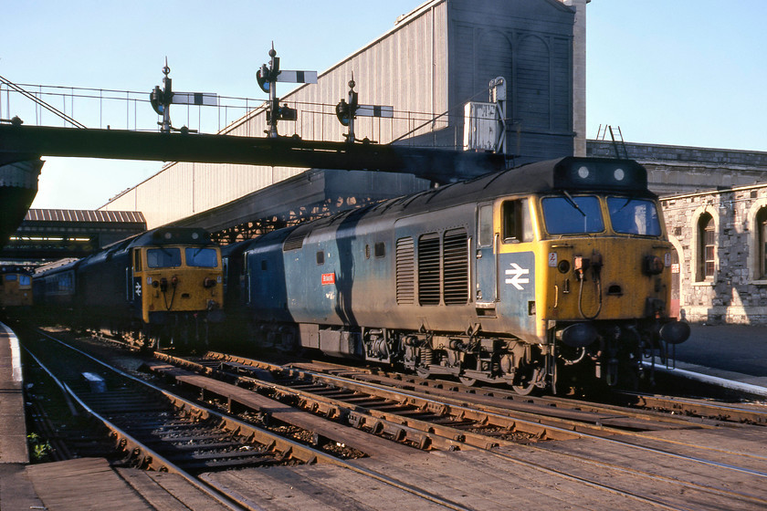 25057, unidentified working, 50025, ECS & 50041, 16.25 London Paddington-Plymouth (1B14), Exeter St. David's station 
 In cracking evening lighting at Exeter St. David's, photograph three of 50041 'Bulwark' shows it leaving with the 16.25 Paddington to Plymouth. Notice that I have had to walk completely off the platform and on to the wooden barrow crossing to take this photograph; can you imagine the rumpus that this would create today? In the shadows to the left of the departing train is 50025 'Invincible' stabled after working a Waterloo service. Finally, to the extreme left, 25057 is seen having just arrived with a train from Barnstaple. 
 Keywords: 25057 50025, ECS 50041 16.25 London Paddington-Plymouth 1B14 Exeter St. David's station Invicible Bulwark