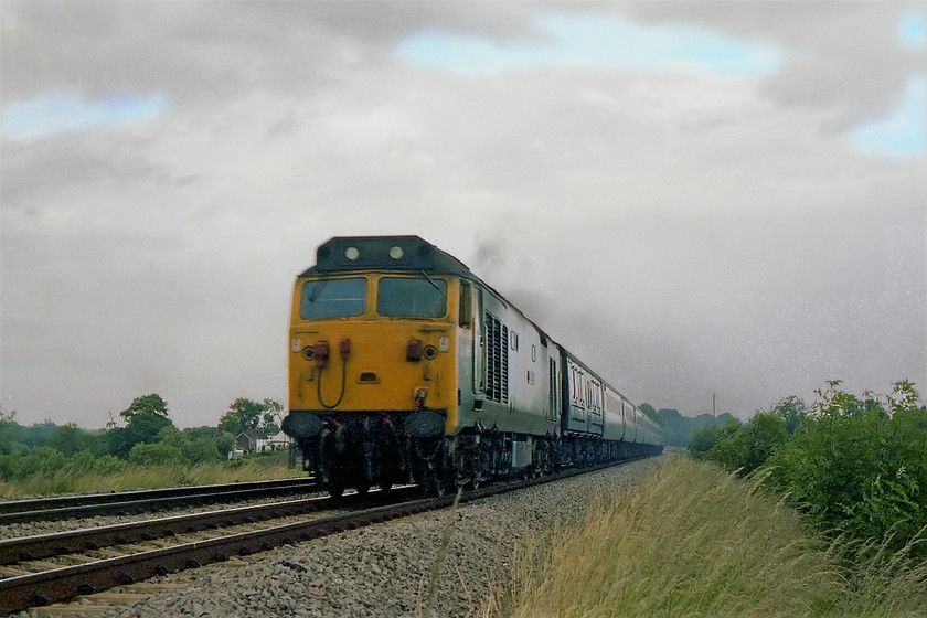 50039, unidentified down working, Woodborough 
 A striking shot of 50039 'Implacable' at full chat on a down express for the West Country. It is seen approaching Woodborough between Westbury and Pewsey. I am not at all sure where I was standing taking this picture but it does not look to be a 'legal' spot as there is no foot crossing just east of the bridge that carries the road into the village of Woodborough itself. Given the very poor lighting, the speed of the train and the Exa camera's maximum 1/150th sec. shutter speed I am amazed how little motion blur there is. The naming process of the 50s was in full swing at this time, 50026 had its 'plates unveiled four days previous to this picture being taken. 
 Keywords: 50039 down working Woodborough