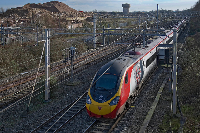 Class 390, 11.33 London Euston-Glasgow Central (1S63), site of Roade station 
 Thee 11.33 Euston to Glasgow Central Virgin service passes the new Roade volcano! The location is the site of the village's old station with the pile rubble being pulverised concrete and bricks from the former Pianoforte factory that used to occupy the land in the background. 
 Keywords: Class 390 11.33 London Euston-Glasgow Central 1S63 site of Roade station Virgin Pendolino