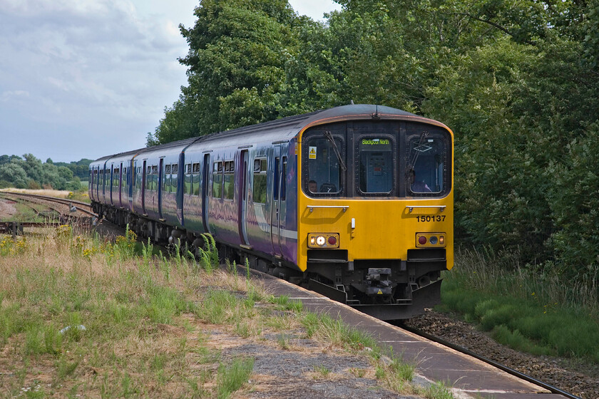 150137, NT 13.22 Manchester Victoria-Blackpool North, Kirkham & Wesham station 
 With the overgrown and fenced-off platform end at Kirkham and Wesham in view, the 13.22 Manchester Victoria to Blackpool North Northern service arrives worked by 150137. With the electrification now approved for this route this scene will change dramatically over the coming few years with extensive re-modelling of the station planned. 
 Keywords: 150137 13.22 Manchester Victoria-Blackpool North Kirkham & Wesham station