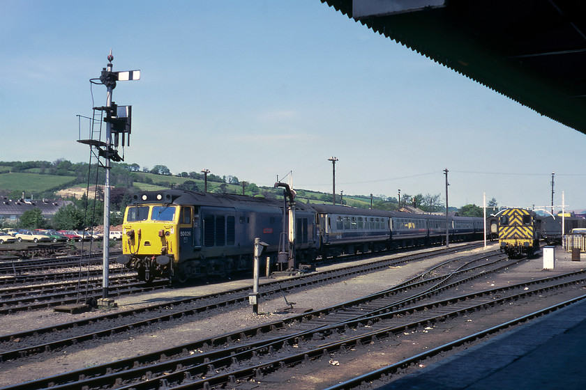 50026, ECS for a London Waterloo working, Exeter Yard 
 50026 'Indomitable' stands at the head of a rake of non air-conditioned Mk.II stock in Exeter Yard. It will have backed into this position after arriving from London Waterloo where it will work back to a little later after the train has been cleaned and serviced. I took a very similar photograph from a passing train in 2015 but the motive power was a little different then, see..... https://www.ontheupfast.com/p/21936chg/29042982204/class-153-class-142-142621-exeter. By 2015, the steam age infrastructure had all gone, including the water crane, the pair of loading gauges and the semaphore with route describer. Close examination of the cars parked to the left of the yard does not reveal them to be staff cars as they are all products of British Leyland and not wearing number plates. They are predominantly brand new Austin Princess' with a couple of Marina estates thrown in for good measure. No doubt they were being stored here by a local garage as it tried in vain to sell them! 
 Keywords: 50026 ECS for a London Waterloo working Exeter Yard Indomitable