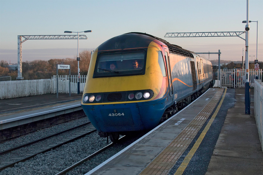 43064, EM 14.34 London St. Pancras-Nottingham (1D43, 14L), Wellingborough station 
 43064 leads the 14.34 St. Pancras to Nottingham hst service through Wellingborough station. The sun was getting very low in the sky by this time of the afternoon but the quality of light is superb! The stanchions for the forthcoming electrification stand high and yet unconnected but, over the next few weeks with an extended Christmas possession the wring will soon be installed changing this scene even further. 
 Keywords: 43064 14.34 London St. Pancras-Nottingham 1D43 Wellingborough station HST East Midlands Railway High Speed Train