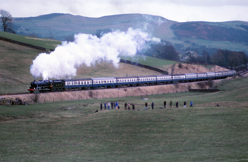 5407, return leg of The Cumbrian Mountains Express, Hellifield-Carnforth, Giggleswick 
 With the outward leg of the Cumbrian Mountain Express having terminated at Hellifiled the much shorter return leg is seen passing Giggleswick near the hamlet of Low Paley Green. The return charter is travelling directly to Carnforth via Wennington and is hauled by former LMS Black Five 5407 (British Railways 45407). Notice the line of enthusiasts who have walked further down the field to take their photographs and record their cine film (no video back then!). This scene is now somewhat different as the A65 Settle/Giggleswick relief road now runs parallel to the railway on the other side to where I am standing. 
 Keywords: 5407 return leg of The Cumbrian Mountains Express Hellifield-Carnforth Giggleswick Black five