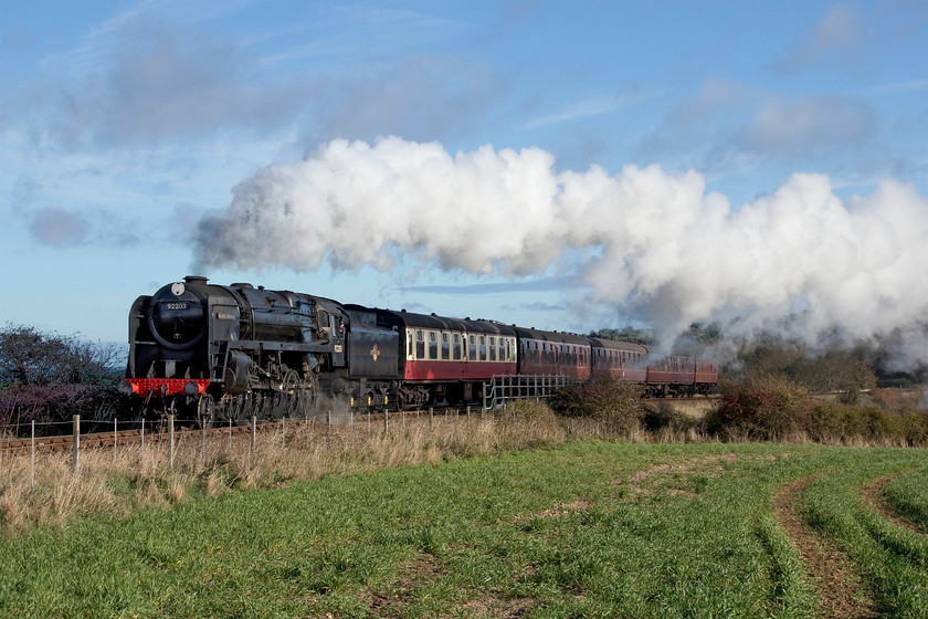 92203, 10.30 Sheringham-Holt, A149 Coast Road bridge 
 The driver of 92203 'Black Prince' opens up the regulator as it climbs the gradient towards Weybourne as it crosses the A149 Coast Road with the North Norfolk Railway's 10.30 Sheringham to Holt service. It's a shame that the the strong north westerly wind has just dragged the exhaust the wrong side of the train, but at least it enhances the curve of the stock. 
 Keywords: 92203 10.30 Sheringham-Holt A149 Coast Road bridge