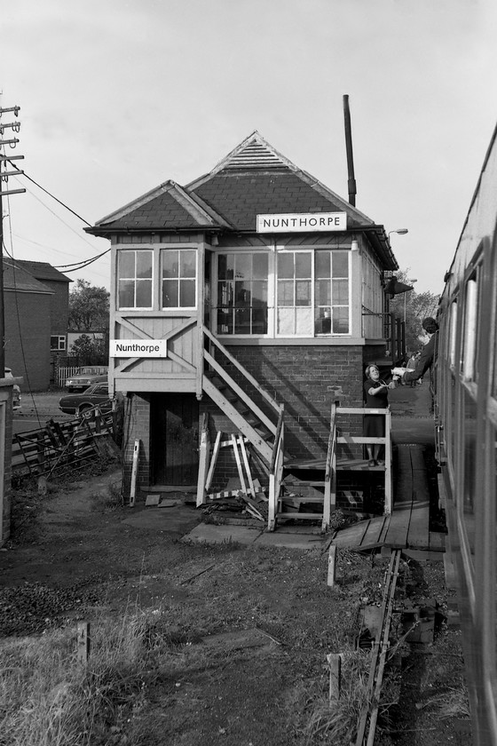 Nunthorpe signal box (NE, 1903) 
 The token is passed from the 10.13 Whitby to Middlesborough DMU to the signalwoman at Nunthorpe. She is standing on a specially constructed platform to enable this to take place at the base of the 1903 North Eastern Railway box. At the time of writing (2020), the box is still in use and controlling the only semaphores in use on the Esk Valley route. Andy and I visited in 2019 and I took a photograph from the level crossing that is seen in the background, see...... https://www.ontheupfast.com/p/21936chg/26273786804/nunthorpe-signal-box I would have been standing about where the 'R' (1976/77) registered Auston Maxi 1750 is standing. 
 Keywords: Nunthorpe signal box NE North Eastern Railway