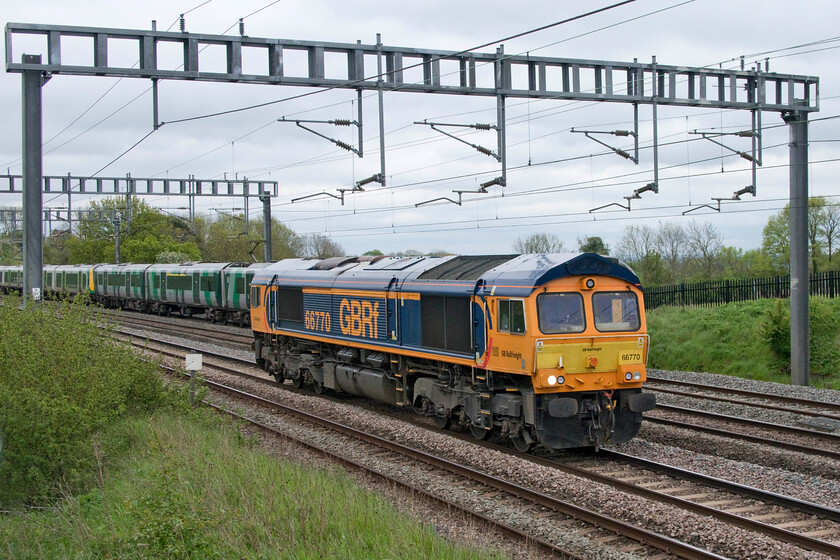 66770, 09.30 Wembley-Bescot Up Engineers (0Z66, 28E), Ashton Road bridge 
 A quick glance at this photograph appears to show 66770 towing a Class 350 unit! However, the unfortunate timing actually shows a London NorthWestern Class 350 Desiro heading north on the down slow passing the GBRf light engine. 66770 was working the 0Z66 09.30 Wembley Yard to Bescot. 
 Keywords: 66770 09.30 Wembley-Bescot Up Engineers 0Z66 Ashton Road bridge