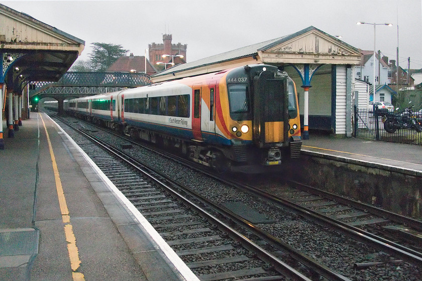 444037 & 444012, SW 13.35 London Waterloo-Weymouth (3W27, 24L), New Milton station 
 It's now 15.30 in the afternoon and the light is absolutely appalling pushing the camera's capabilities to the limit! 444037 and 444012 arrive at New Milton station working the 13.35 Waterloo to Weymouth service. In the background is New Milton's famous 1900 built mock Tudor style water tower constructed from locally sourced, cut and finished orange-red coloured bricks. 
 Keywords: 444037 444012 13.35 London Waterloo-Weymouth 3W27 New Milton station SWR South Western Railway