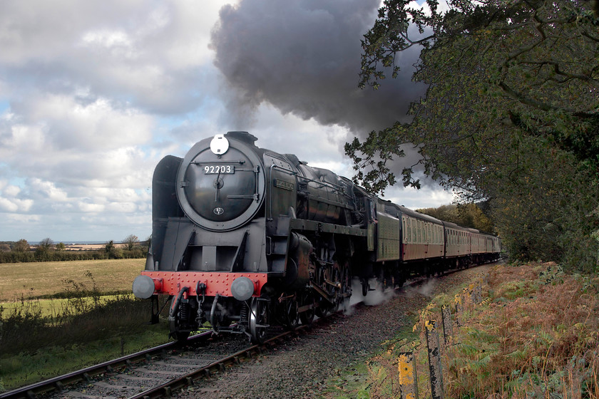 92203, 10.30 Sheringham-Holt, Kelling woods 
 92203 'Black Prince' gets into its stride as climbs Kelling Bank working the 10.30 Sheringham to Holt. A big and powerful 9F such as this would have no problem ascending the 1:80 bank from a standing start with such a light load but it still sounds great! 
 Keywords: 92203 10.30 Sheringham-Holt Kelling woods