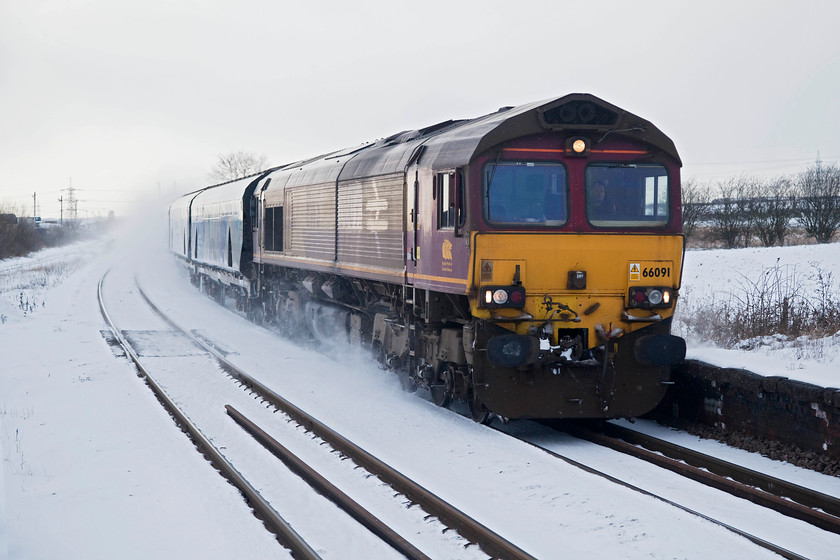 66091, 16.04 Milford West-Drax Power Station, Whitley Bridge station 
 66091 throws up plumes of snow as it sweeps through Whitley Bridge station working the 16.04 Milford West to Drax Power Station BIOMAS train. Notice that somebody has attempted to change 66091's livery into British Rail large logo! With the light virtually gone, just time for one more station and then a turn for home. Hopefully, the weather would cause no problems on the journey! 
 Keywords: 66091Whitley Bridge station