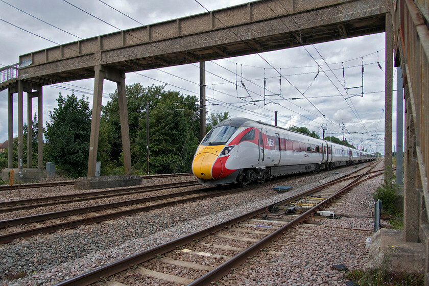 800105, GR 09.45 Leeds-London King's Cross (1A20, 1E), Tallington 
 I utilised the widest angle from the lens to compose this slightly different image of 800105 working the 09.45 Leeds to King's Cross LNER service passing Tallington. Due to the extremely wide angle, I had to utilise Photoshop's transition's functions to straighten out the curves of the verticals. I wonder if the concrete footbridge that was installed when the line was electrified in 1987 was manufactured at the adjacent Dowmac plant to which rail access is gained via the points and track verging off to the right in this photograph. 
 Keywords: 800105 09.45 Leeds-London King's Cross 1A20 Tallington LNER AZuma