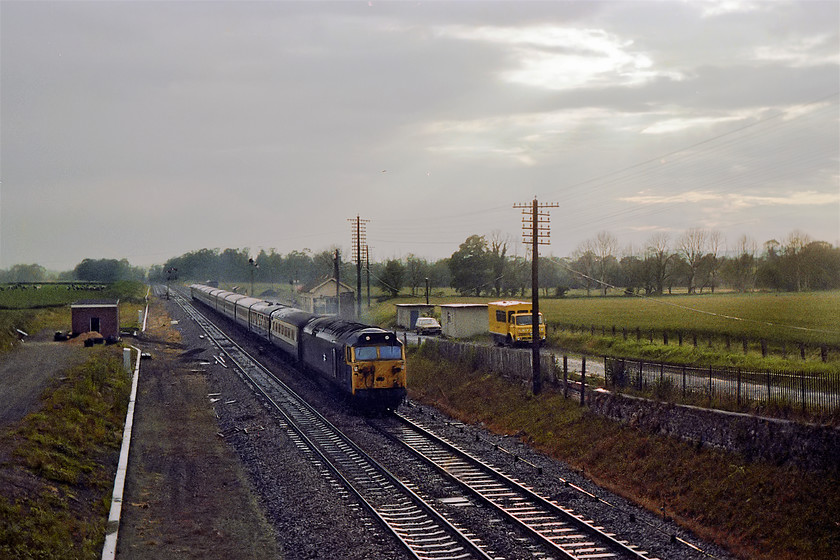 50032, unidentified up working, Woodborough 
 After a torrential summer rainstorm 50032 (yet to be named) hammers eastwards past Woodborough signal box with a Paddington Express. This image shows evidence of things to come. Notice the recently constructed relay room to the left and various other rationalisation works taking place. The West of England MAS programme was in full flow and this box was in its final year of operation. However, interestingly the relief lines remained and have actually been added to making it a short four-track section complete with other refuge sidings. Notice the distinctively bright yellow British Rail Leyland crew truck and, parked behind it, the signalman's Austin Allegro estate. Finally, glance away from the railway to the fields behind, notice the line of dead elm tress that had been killed by Dutch elm disease that had totally blighted the West Country landscape. 
 Keywords: 50032 up working Woodborough