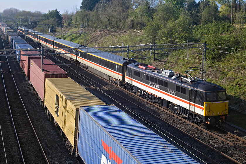 87002, outward leg of The Emerald Isle Express, 07.00 London Euston-Holyhead (1Z90, 4L) & 03.10 Felixstowe North-Trafford Park (4M18, 4L), Victoria bridge 
 Making a fine sight as it catches the morning sunshine 87002 Royal Sovereign leads LSLs immaculate and authentically repainted set of Mk. III stock passing Victoria bridge between Roade and Ashton in Northamptonshire. The LSL charter was running as 1Z90 throughout with heritage ScotRail 47712 Lady Diana Spencer taking over at Crewe. This was an unadvertised charter that I had totally missed until somebody popped some timings up on a forum. It was a one-way journey for customers that was the first leg of a wider tour of Ireland returning, I believe, by air. As it passes this spot, the 4M18 Freightliner is seen in the foreground 
 Keywords: 87002 The Emerald Isle Express, 07.00 London Euston-Holyhead 1Z90 03.10 Felixstowe North-Trafford Park 4M18 Victoria bridge Intercity Swallow Royal Sovereign