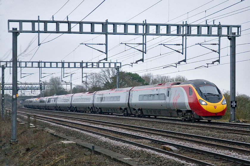 Class 390, VT 07.23 London Euston-Birmingham New Street, Ashton Road bridge 
 The 07.23 Euston to Birmingham New Street Pendolino sweeps past Ashton Road bridge just south of Roade in Northamptonshire. Note the black and white sign attached to the electrification mast. This indicates to trackworkers of limited clearance caused, in this particular case, a steep embankment dropping away to the right of the down fast line. 
 Keywords: Class 390 07.23 London Euston-Birmingham New Street Ashton Road bridge Virgin Pendolino