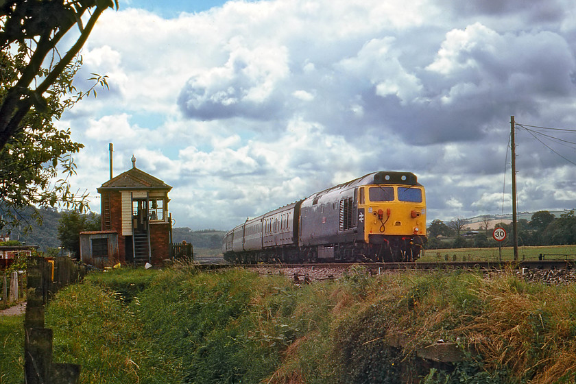 50012, 13.48 Plymouth-London Paddington (1A03), Stoke Canon 
 50012 'Benbow' is seen passing the Stoke Canon Signal Box and level crossing with the 1A03 13.48 Plymouth to London Paddington. 'Benbow' was one of the five class 50s that ended up at Vic Berrys scrap yard in Leicester. I am not sure it was ever at the top of the infamous stack of scrap engines that feature in so many contemporary photographs. It looks like I am in for a soaking if the black cloud rolling in from the west is anything to go by! 
 Keywords: 50012 13.48 Plymouth-London Paddington 1A03 Stoke Canon