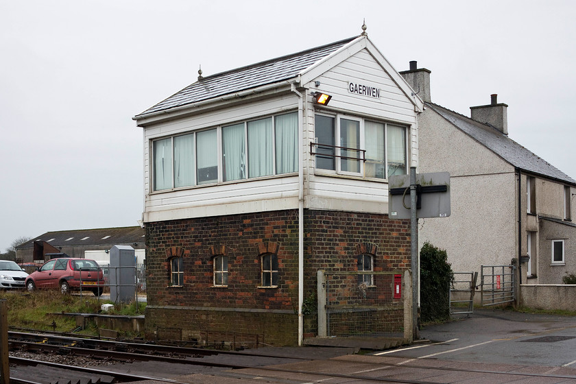 Gaerwen Signal Box (LNWR, 1882) 
 Despite having had some modernisation work undertaken, not least of which is the UPVC cladding, the Gaerwen signal box retains its slate roof and finials. Constructed by the LNWR in 1882 it controls the level crossing in the village and controls the junction with the mothballed Almwch branch. There was once a station located to the left of the box in this image where the cars are, it closed in 1966. Notice the post box integrated into the signal box wall. 
 Keywords: Gaerwen Signal Box