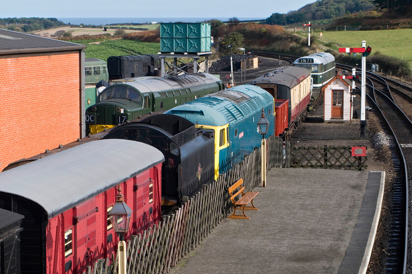 E56062, 12131, D6732, 47367, Gresley Buffet E9128 & D5631, stabled, Weybourne Yard 
 With a blue sky and the North Sea in the background, what could be better? An eclectic lineup of locomotives and stock are seen from Weybourne station's footbridge. There's a Class 101 DMU coach, M56062 coupled up to shunter D12131 partially obscured by D6732. D5631 is seen at the end of the line nearest the camera with Gresley buffet car E9128 and on-loan 46367 'Kenny Cockbird'. The red timber van to the left is used by the excellent station bookshop Unfortunately only open on Saturday Sunday during the season) for storage. 
 Keywords: E56062 12131 D6732 47367 Kenny Cockbird Gresley Buffet E9128 stabled, Weybourne Yard & D5631